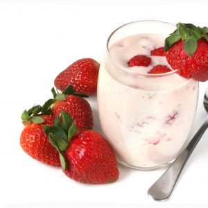 Glass of strawberry yoghurt, with fresh strawberries and a spoon.