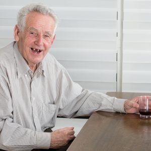 Old man holding glass with alcohol dring and laughing laudly